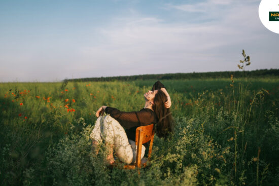 A woman enjoys a serene moment sitting among vibrant flowers in a peaceful field, embodying the essence of slow living.