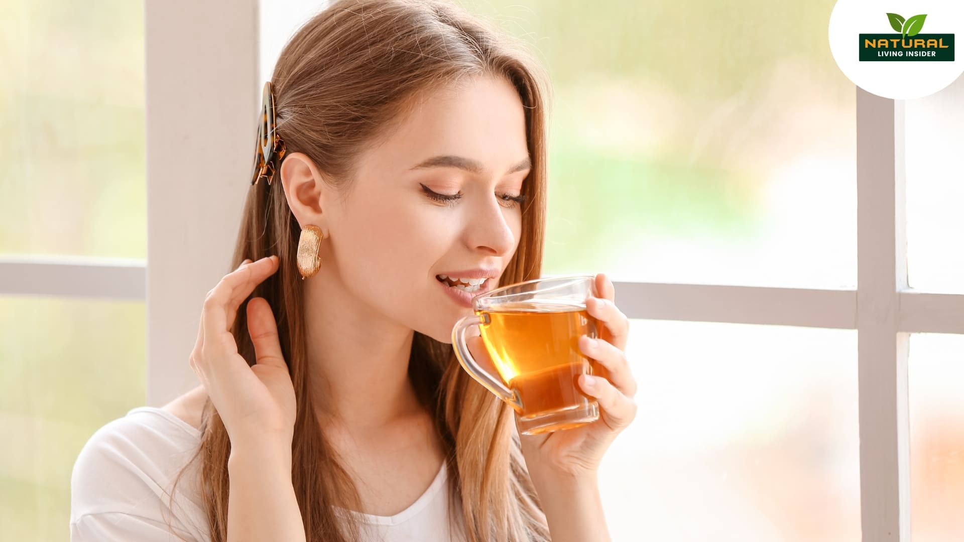 A woman sips tea peacefully in front of a window for glowing skin, surrounded by soft light and a tranquil setting.