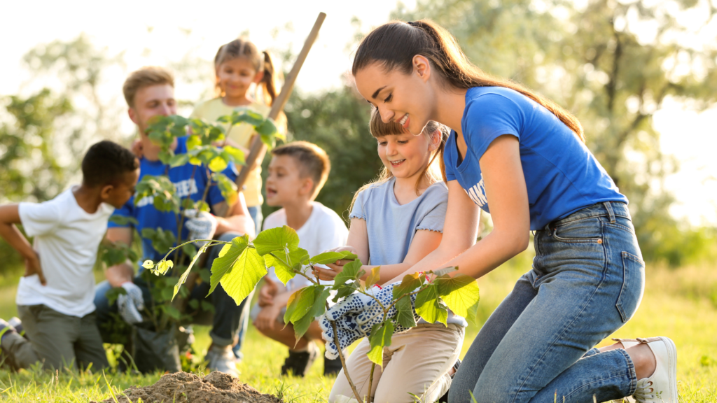 A group of children enthusiastically planting young trees in a grassy area, promoting environmental awareness and teamwork.