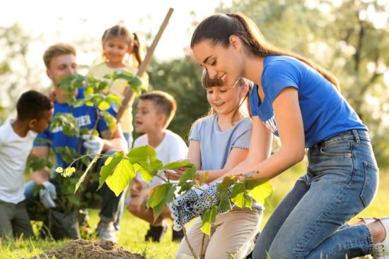 A group of children enthusiastically planting young trees in a grassy area, promoting environmental awareness and teamwork.