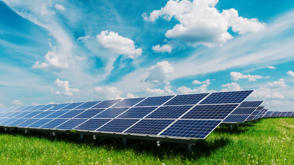 Solar panels installed in a field under a clear blue sky adorned with fluffy white clouds.