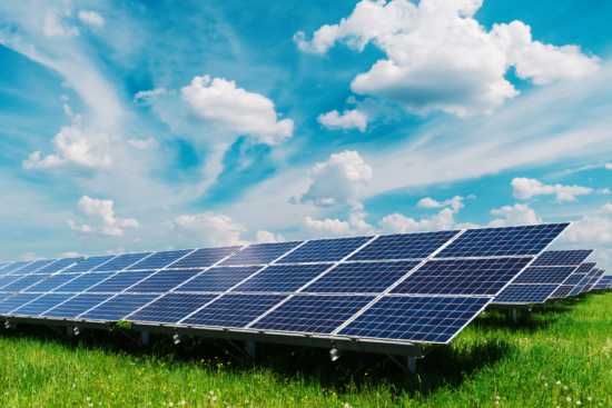 Solar panels installed in a field under a clear blue sky adorned with fluffy white clouds.