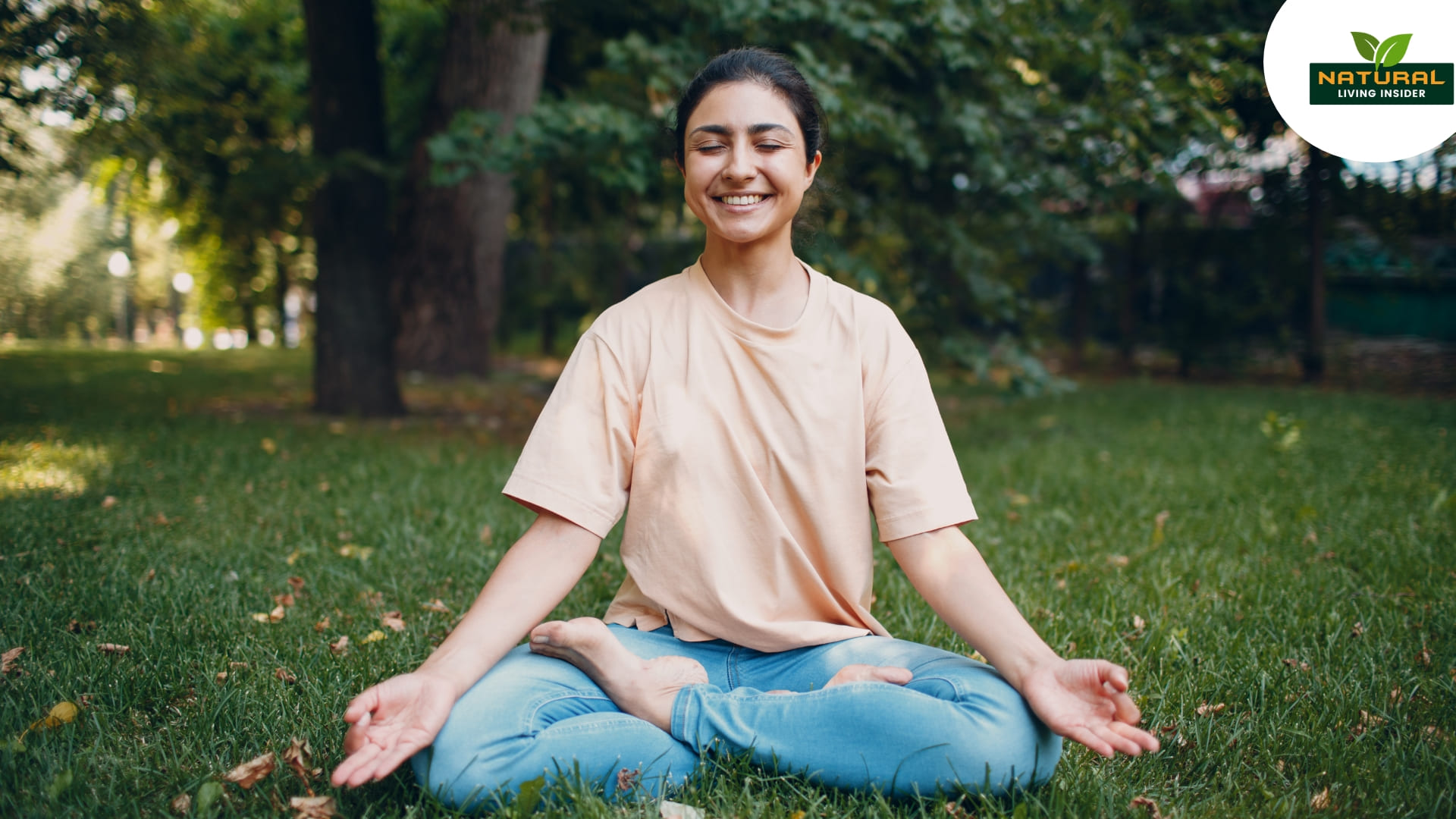 A woman peacefully meditates in a grassy field, embodying natural fitness.