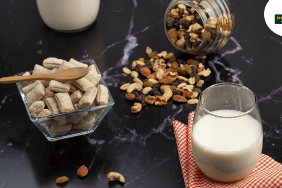 A glass of milk beside a bowl of nuts and a spoon, showcasing a quick and nutritious snack option.