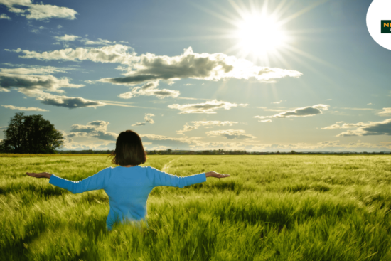 A woman in a field, arms wide, embracing natural harmony and health.